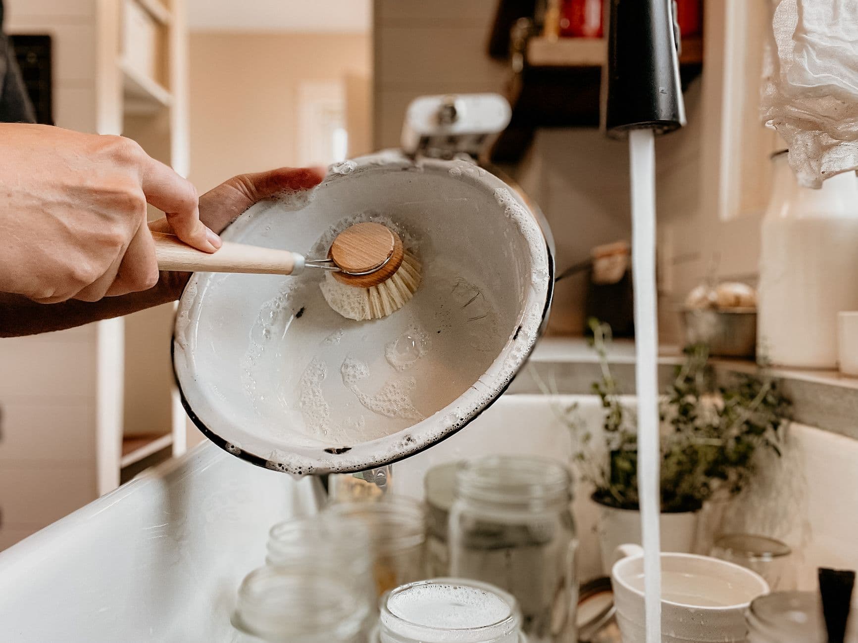 A person washing a bowl with a scrubbing brush at a kitchen sink