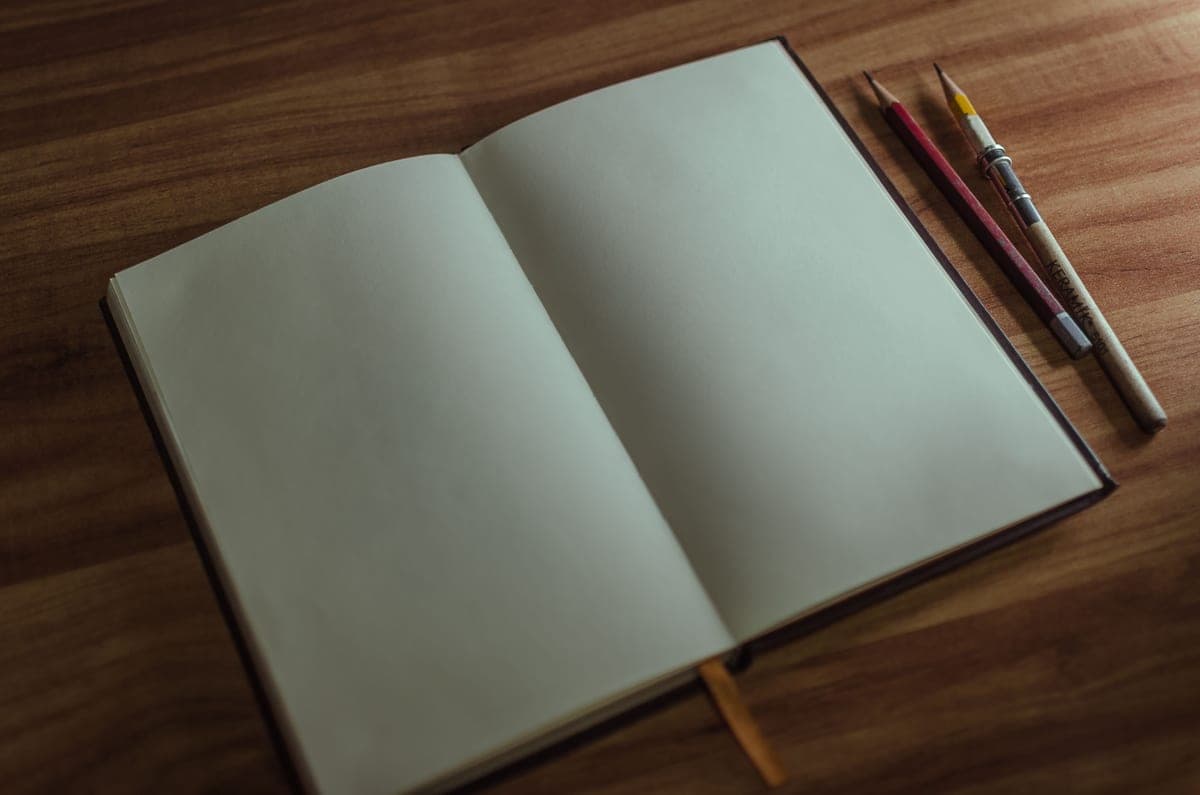 An open notebook and pencils on a wooden desk